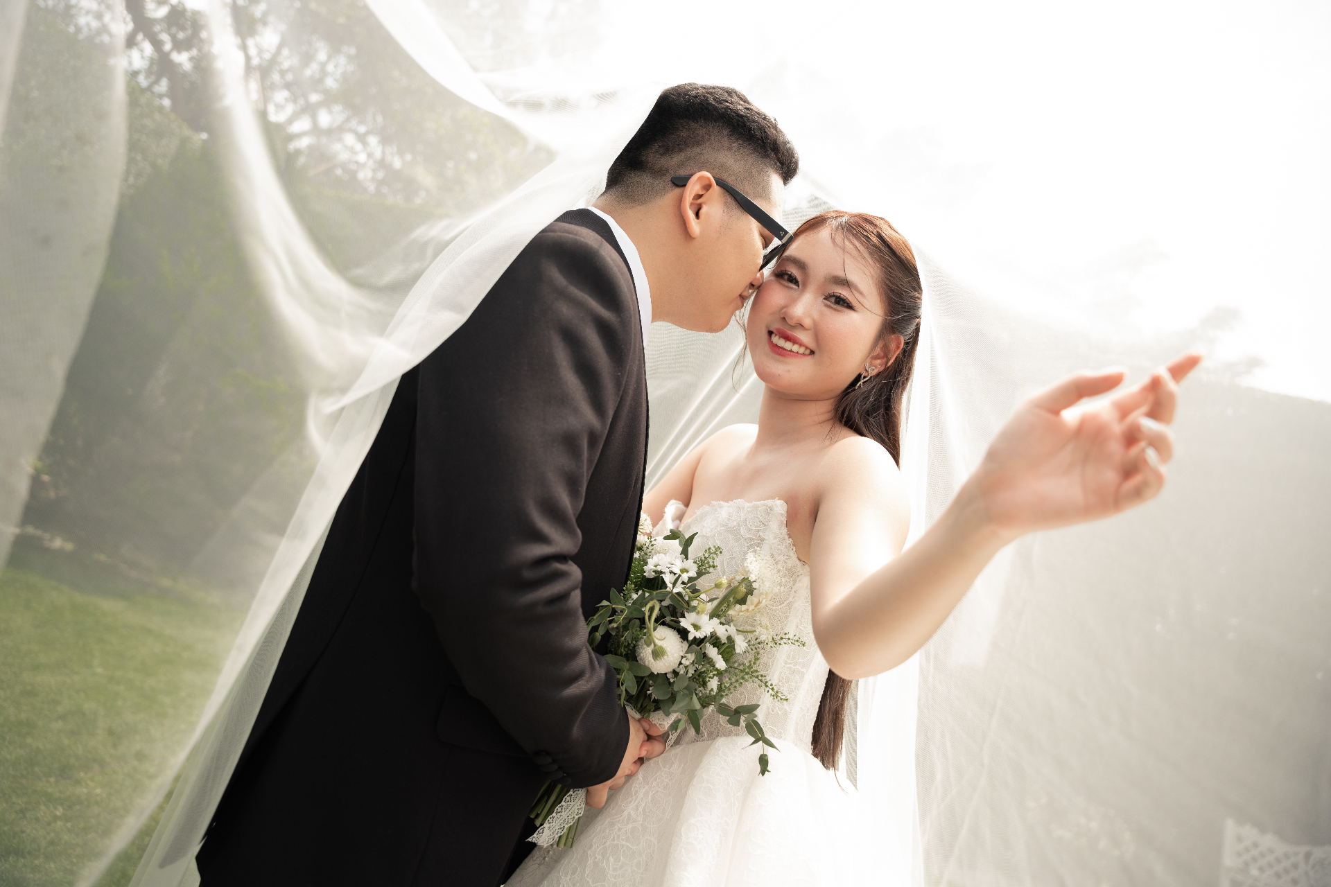 Chú rể hôn nhẹ lên má cô dâu dưới voan cưới