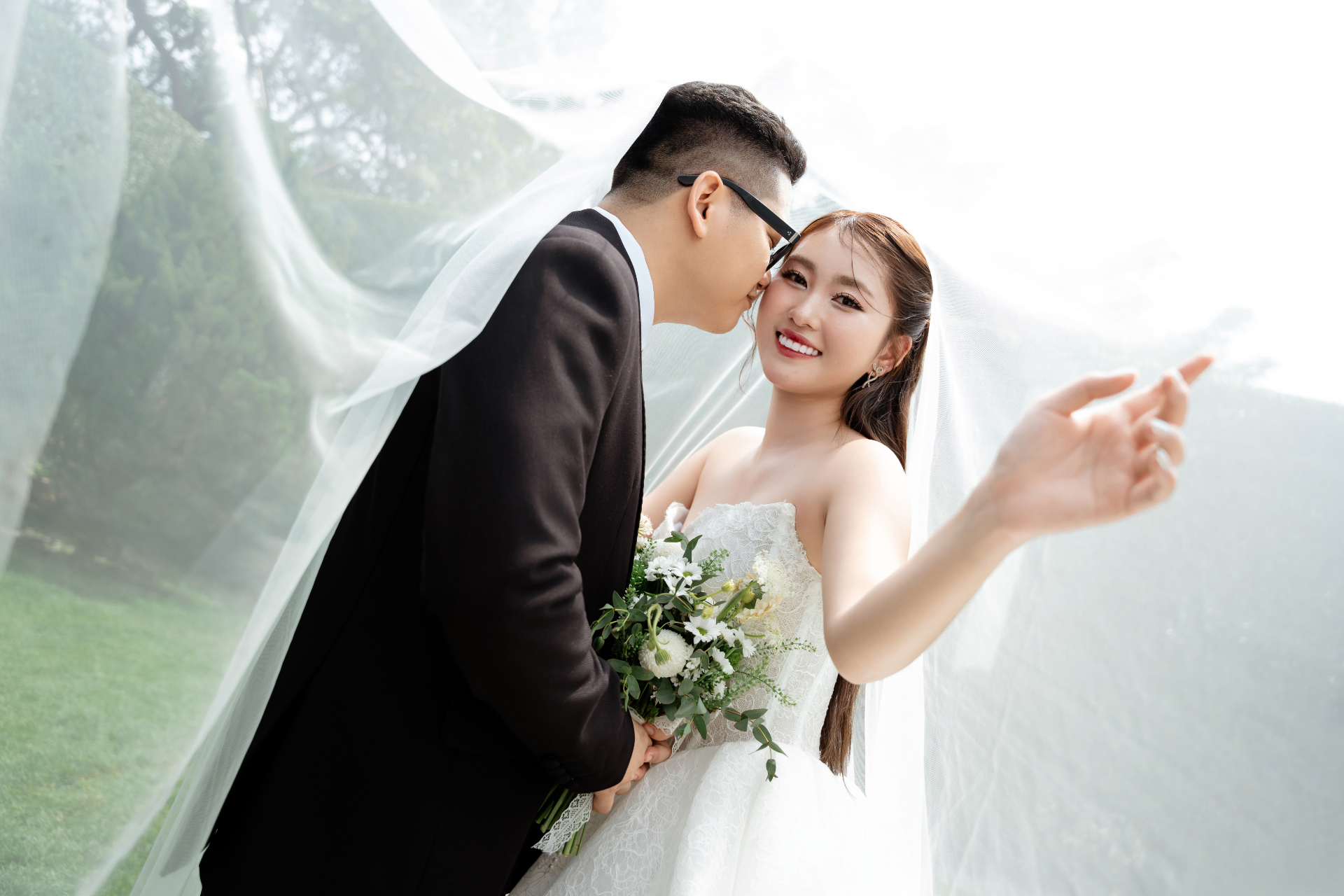 Chú rể hôn nhẹ lên má cô dâu dưới voan cưới